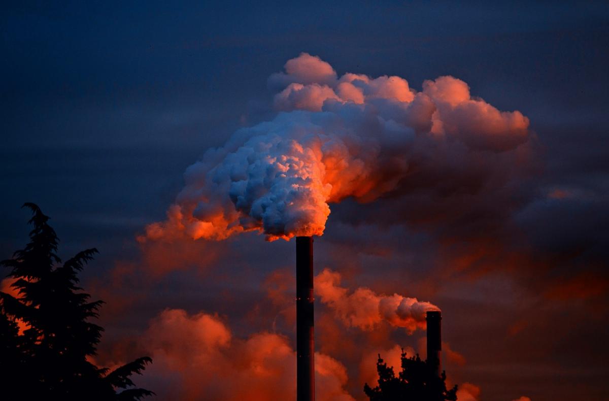 A chimney emits a thick cloud of gas at sunset.