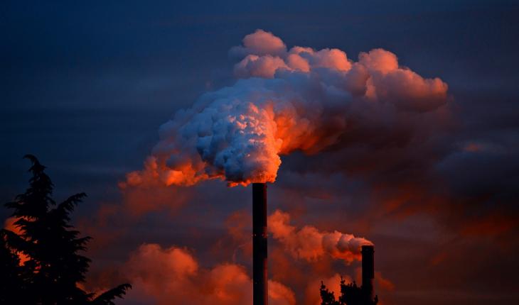 A chimney emits a thick cloud of gas at sunset.