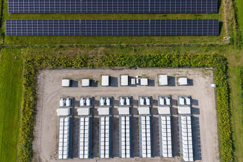 Aerial view of a large-scale solar farm featuring extensive rows of photovoltaic panels and a battery energy storage system in the rural landscape of Wanneperveen